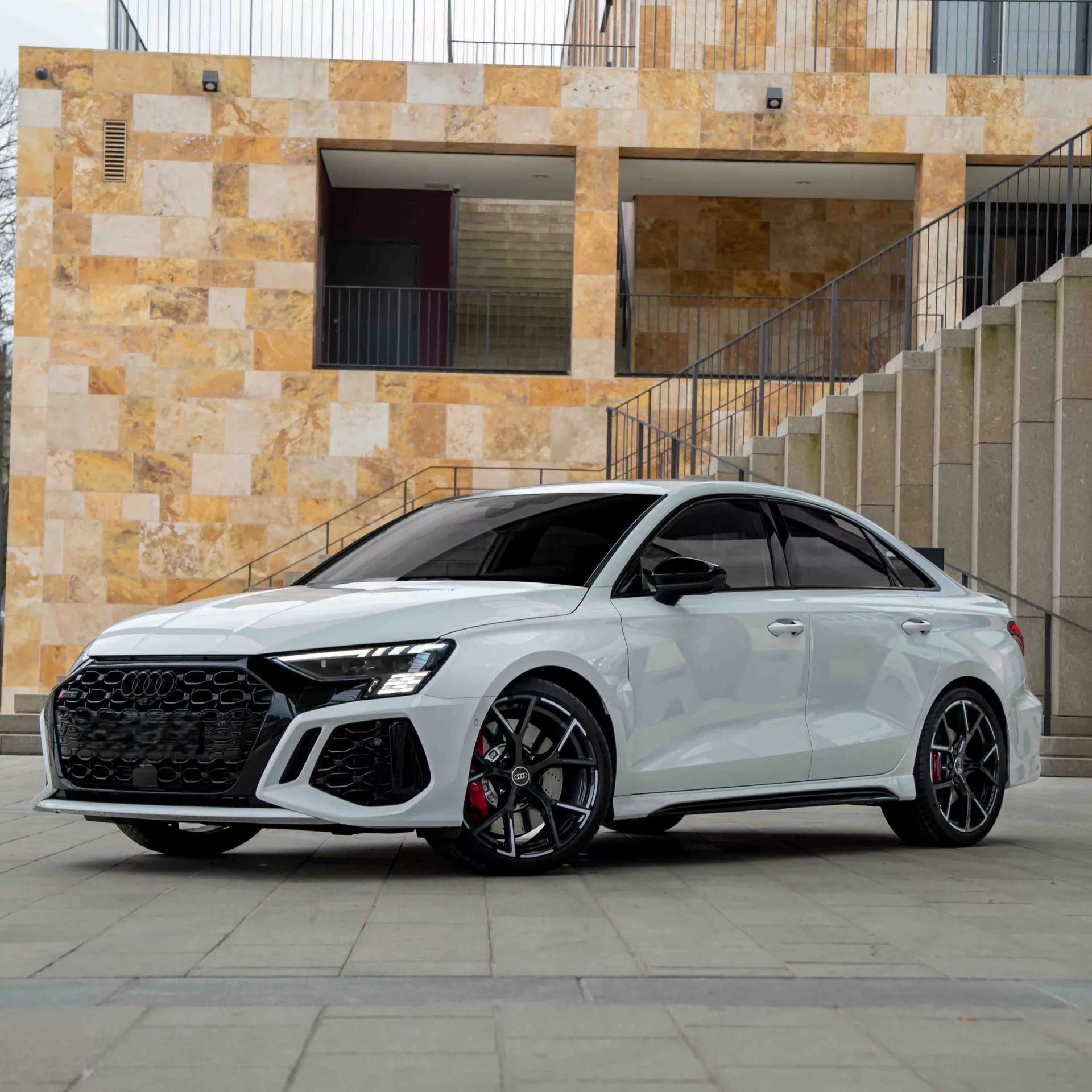Audi RS3 Limousine in Weiß, Seitenansicht vor Treppen mieten.
