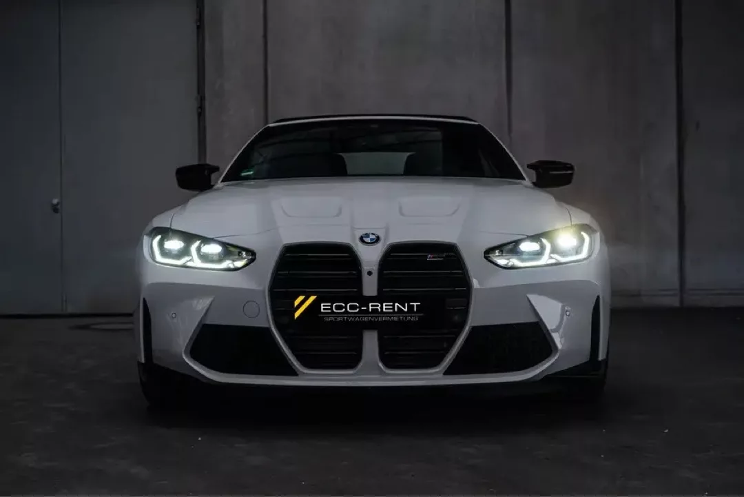 Weißes BMW M4 Cabrio Competition mit eingeschaltetem Frontlicht in einer Garage.