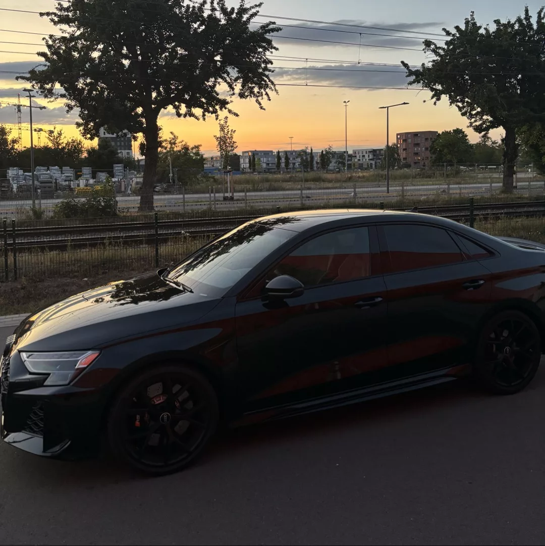 Schwarzer Audi RS3 bei Sonnenuntergang auf einer Straße geparkt.
