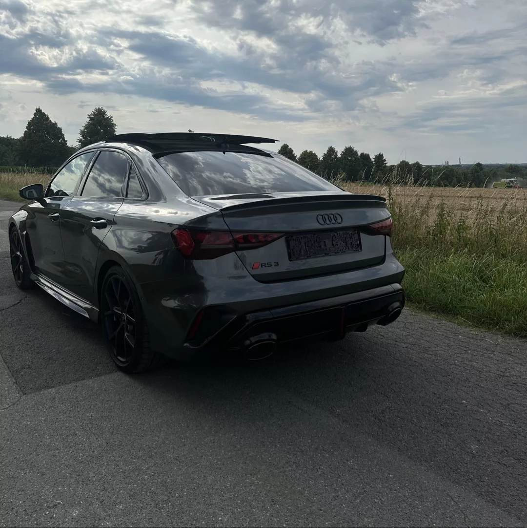 Audi RS3 Limousine in Grau von hinten auf Landstraße mieten.