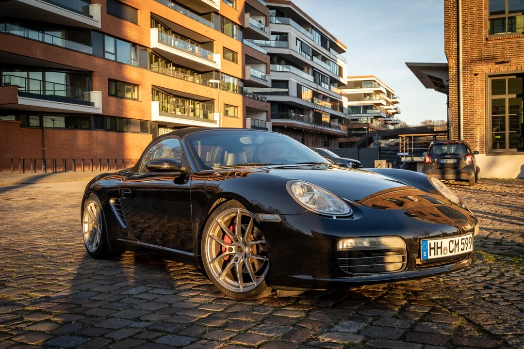 Porsche 987 Boxster S Cabrio in Schwarz mieten - Seitenansicht auf Kopfsteinpflaster.
