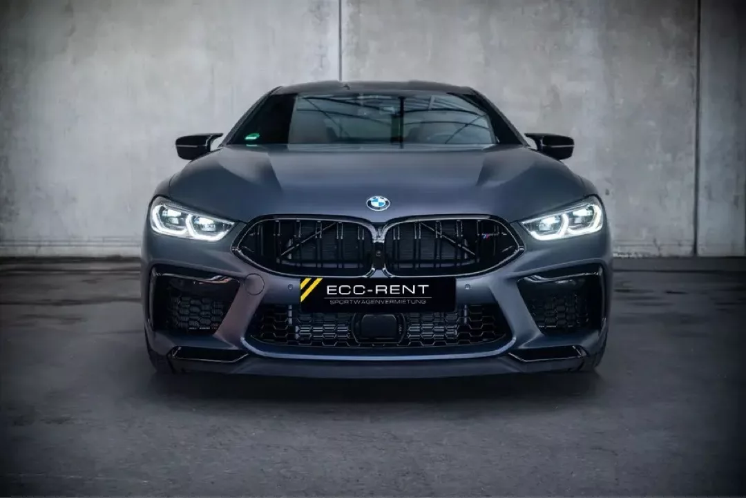 BMW M8 Gran Coupé in dunklem Grau, Frontansicht vor einer Betonwand.