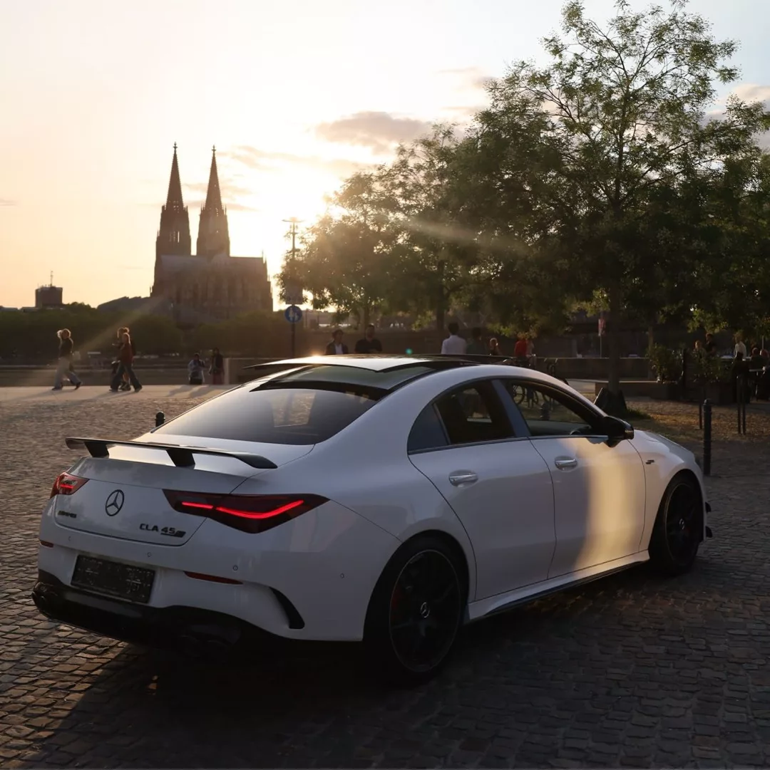 Ein weißer Mercedes AMG CLA45s 4M+ steht bei Sonnenuntergang auf einer gepflasterten Straße.