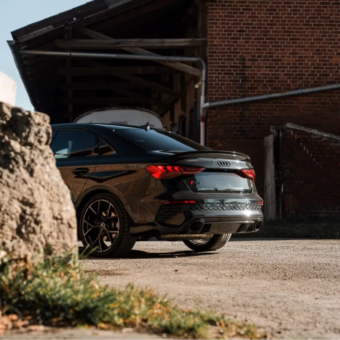 AUDI RS3 Limousine in Schwarz, Heckansicht auf Schotterweg, mieten.