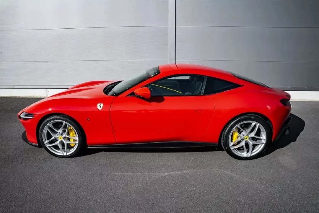 Roter Ferrari Roma seitlich vor grauer Wand geparkt.