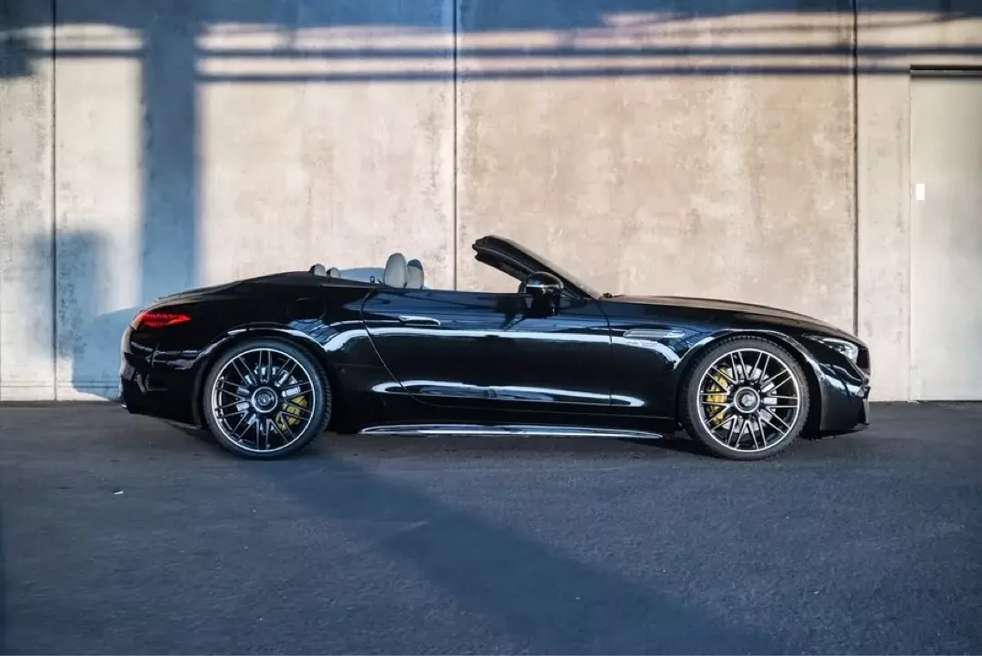 Schwarzer Mercedes-Benz SL63 AMG Roadster mit offenem Verdeck vor einer Betonwand.