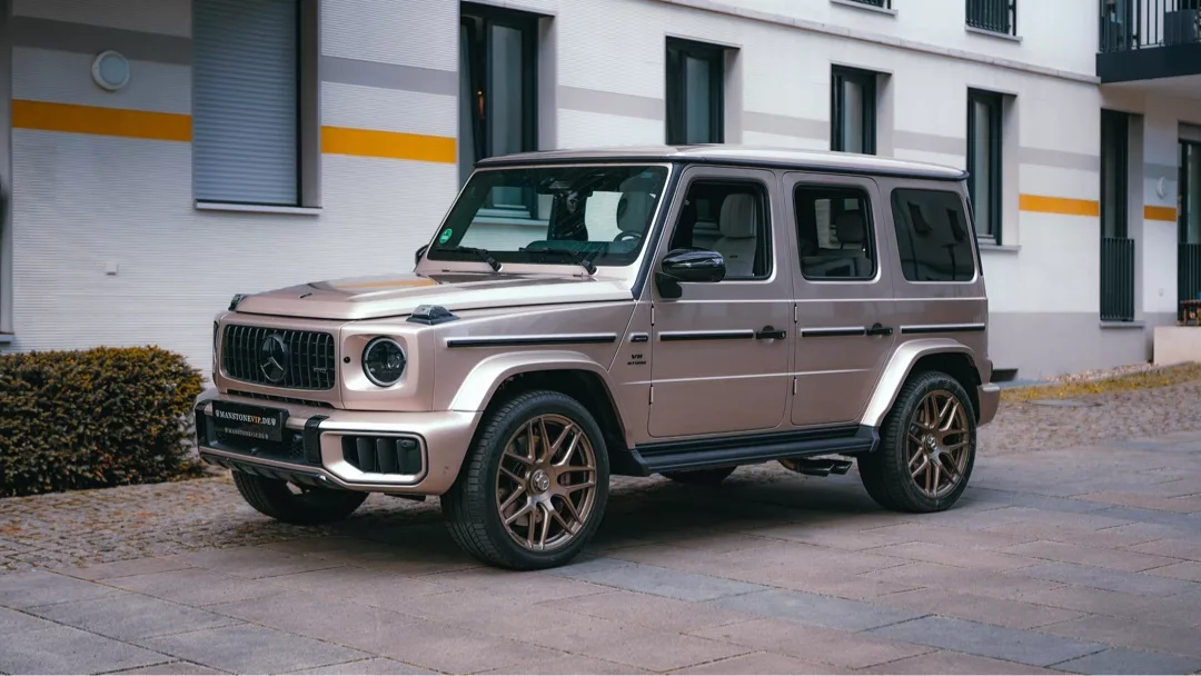 Mercedes-Benz G63 AMG 2025 in Beige, Seitenansicht vor Gebäude mieten.