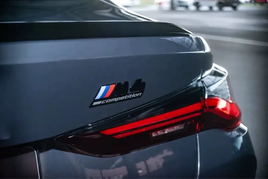 Rückansicht eines BMW M4 Competition mit Logo und leuchtendem Rücklicht.