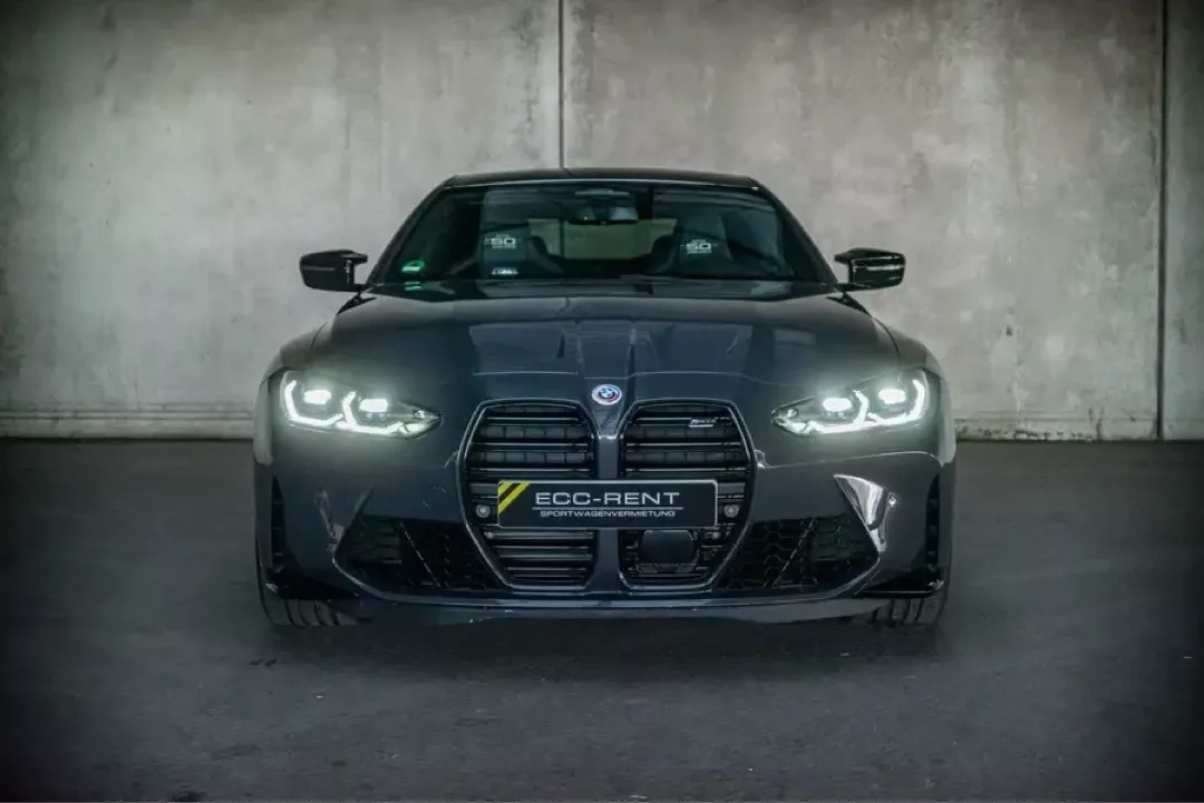 BMW M4 Competition in Dunkelgrau vor Betonwand, Frontansicht.