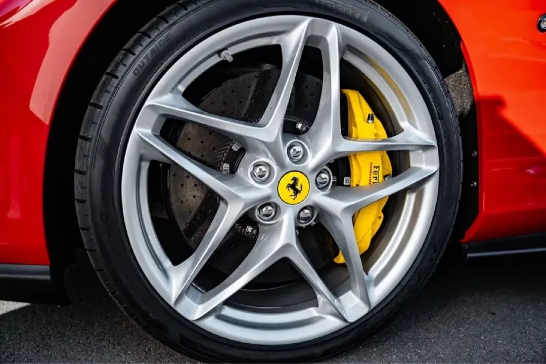 Nahaufnahme einer silbernen Felge mit gelber Bremse eines roten Ferrari Roma.
