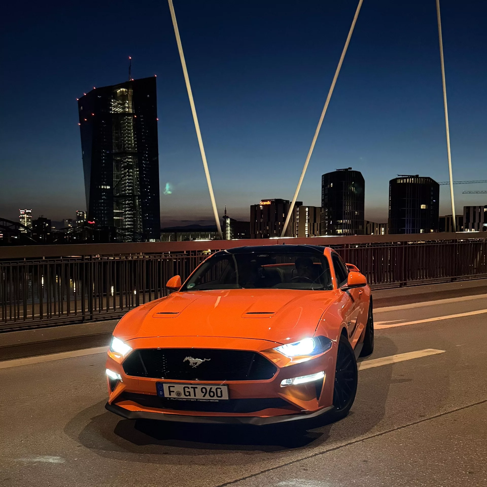 Ford Mustang GT in Orange bei Nacht mieten - Frontansicht auf Brücke