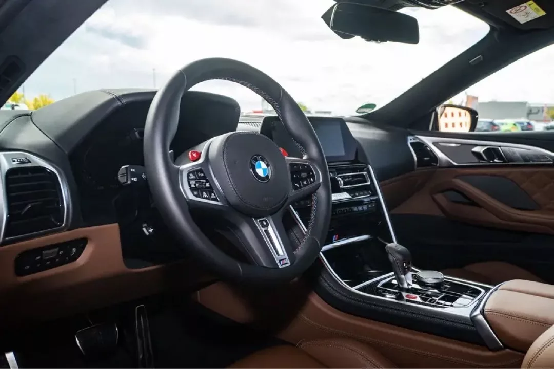 Innenraum eines luxuriösen BMW M8 Gran Coupé mit modernem Cockpit und brauner Lederausstattung.