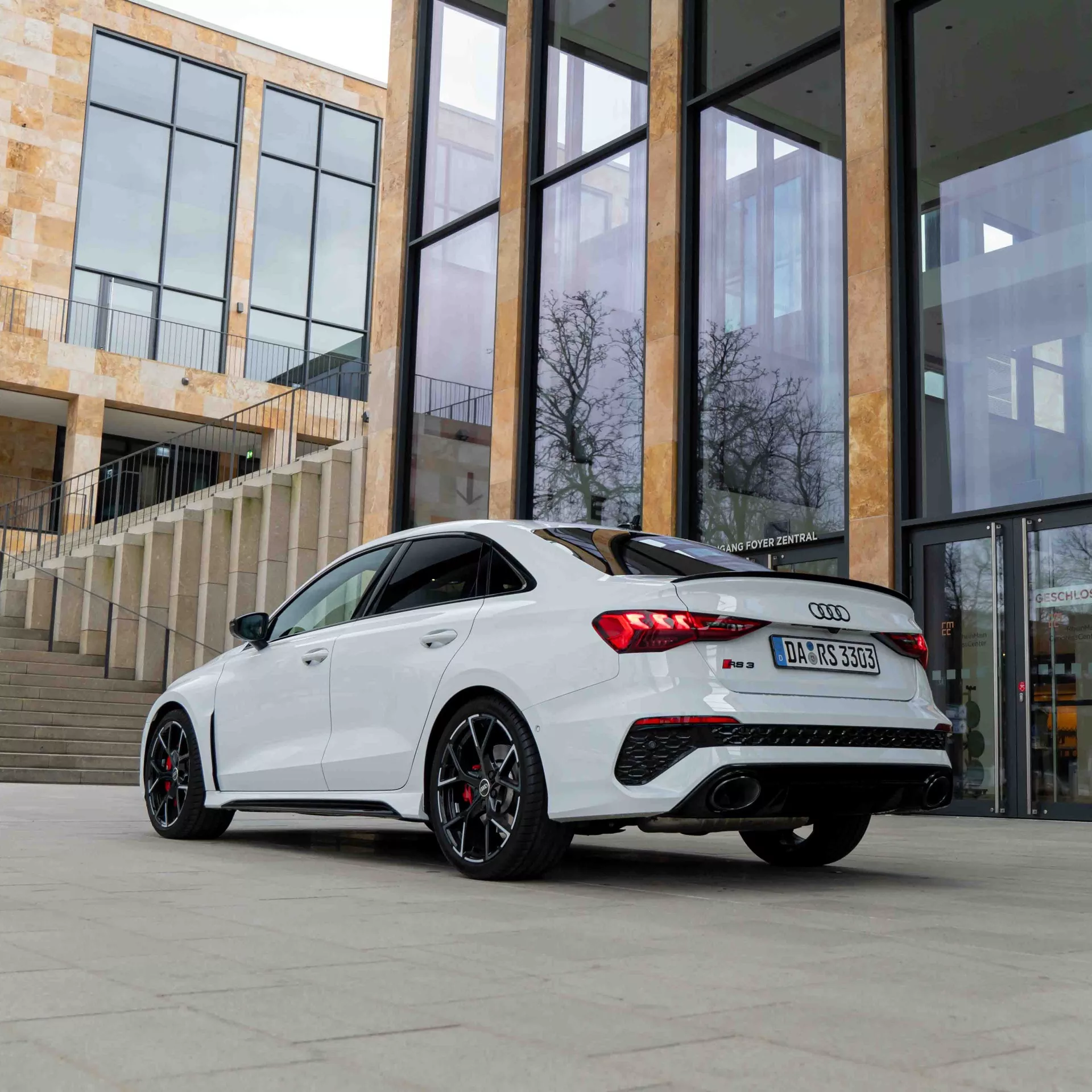 Audi RS3 Limousine in Weiß, Rückansicht vor modernem Gebäude mieten.