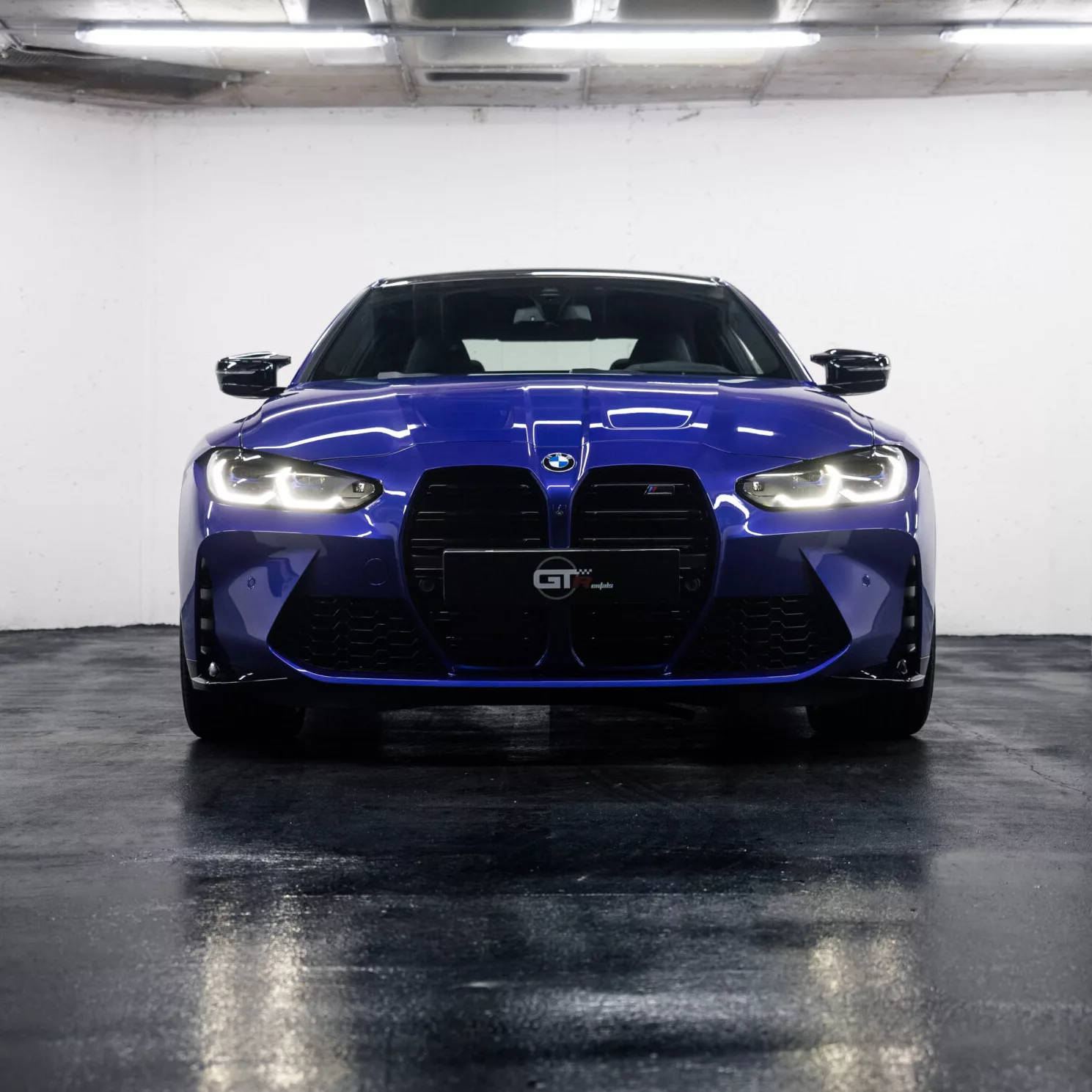 Blauer BMW M4 Competition von vorne in einem Parkhaus.