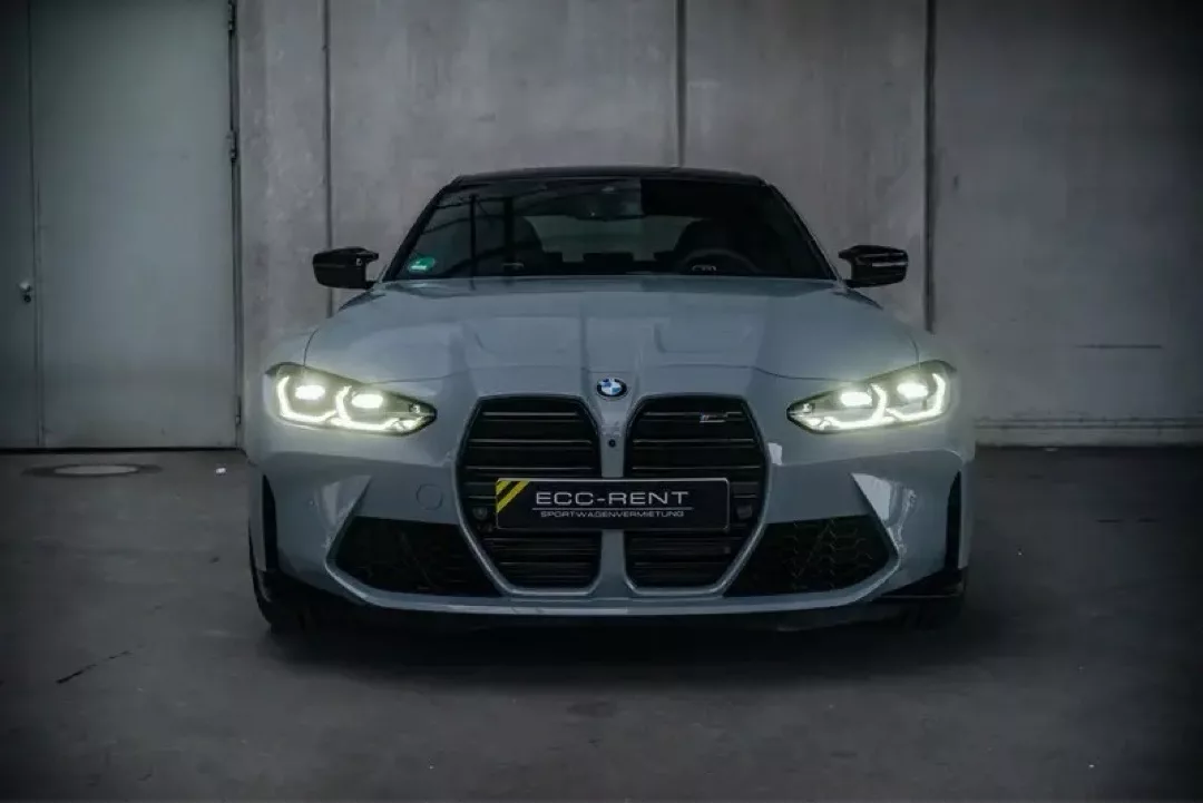 Frontansicht eines BMW M3 Competition in einer Garageneinfahrt, mit eingeschaltetem Abblendlicht.