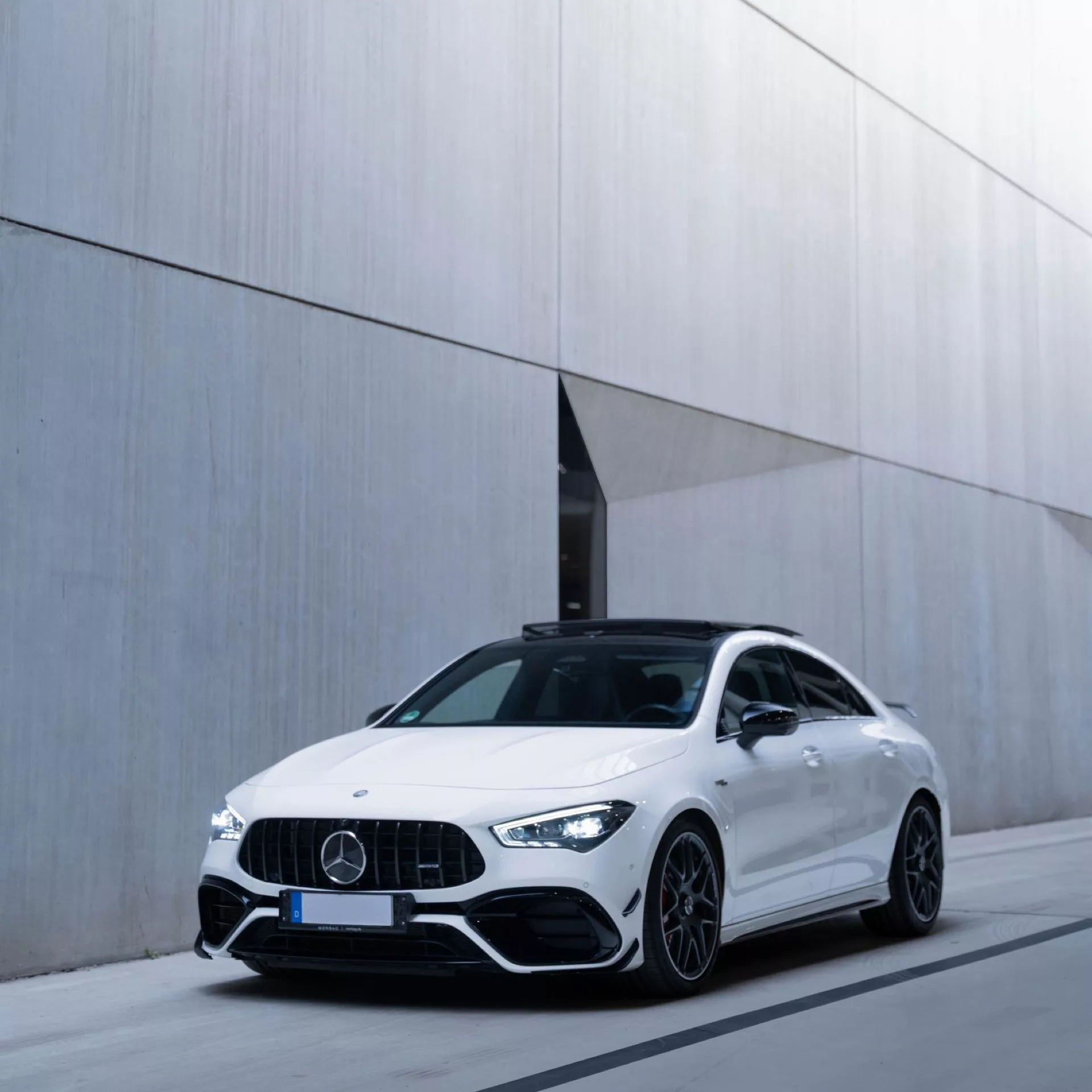 Weißer Mercedes AMG CLA45s 4M+ vor modernem Gebäude.