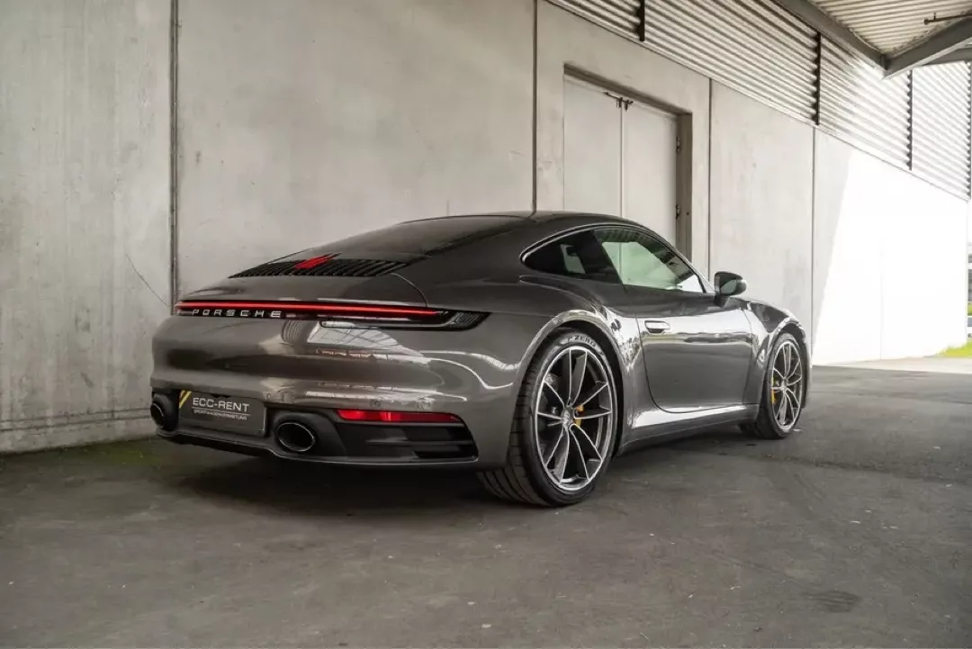 Grauer Porsche 911 Carrera S (992) in seitlicher Heckansicht unter überdachter Struktur.
