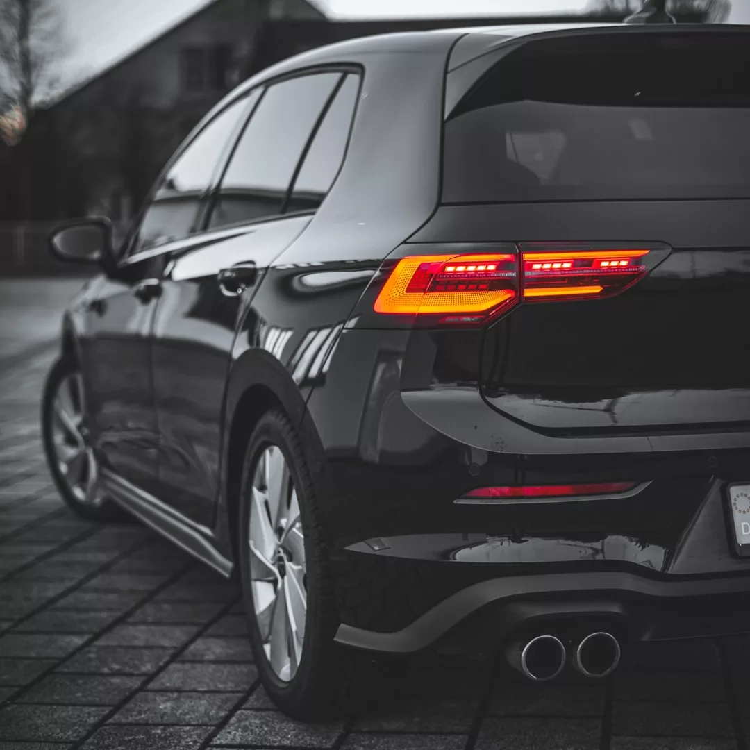 Schwarzer VW Golf 8 GTD auf gepflasterter Fläche mit eingeschalteten Rücklichtern.