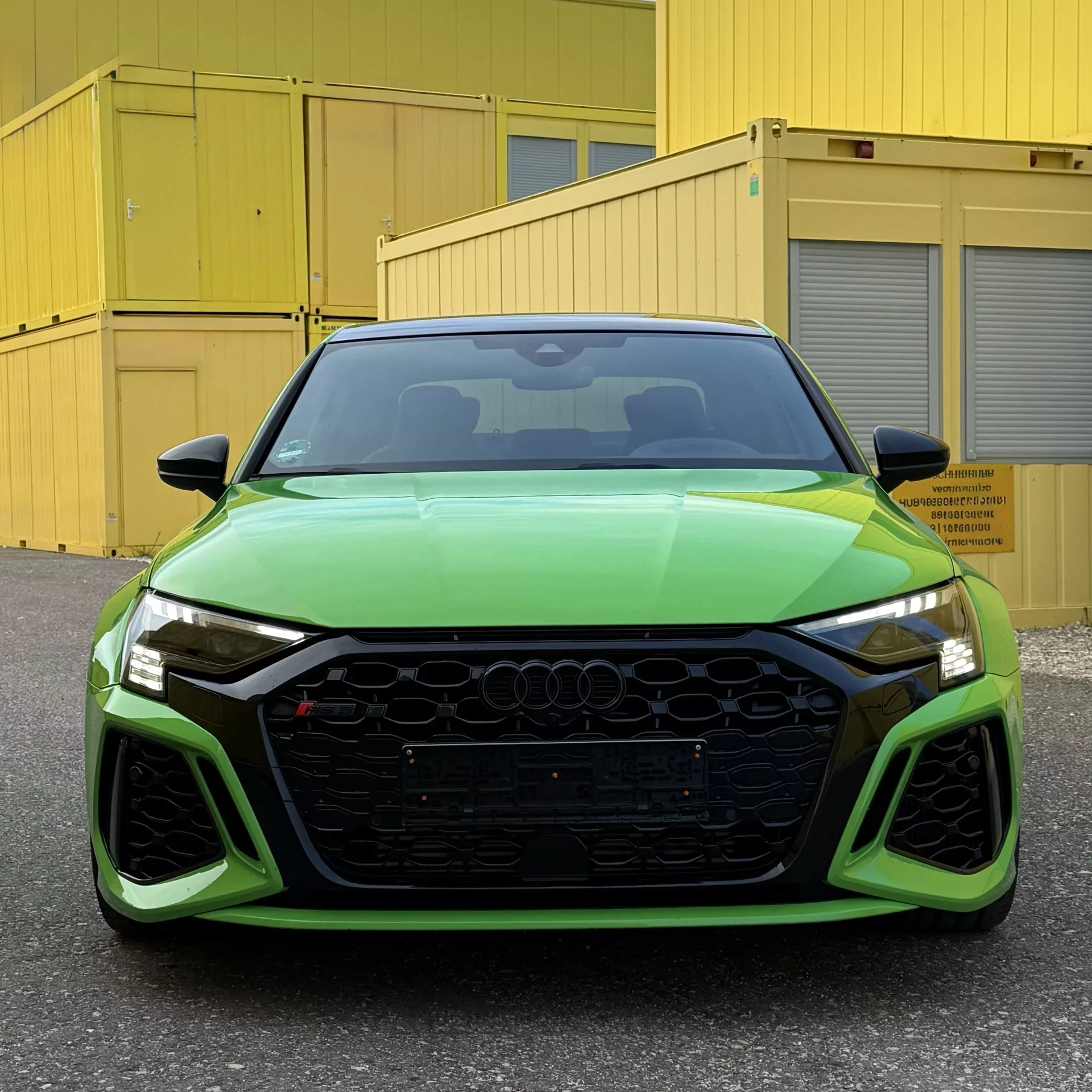 Audi RS3 in Grün, Frontansicht vor gelben Containern mieten.