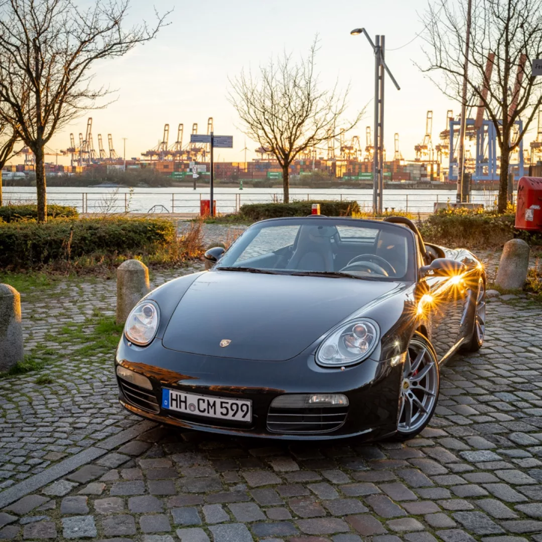 Porsche 987 Boxster S Cabrio in Schwarz mieten - Frontansicht bei Sonnenuntergang.