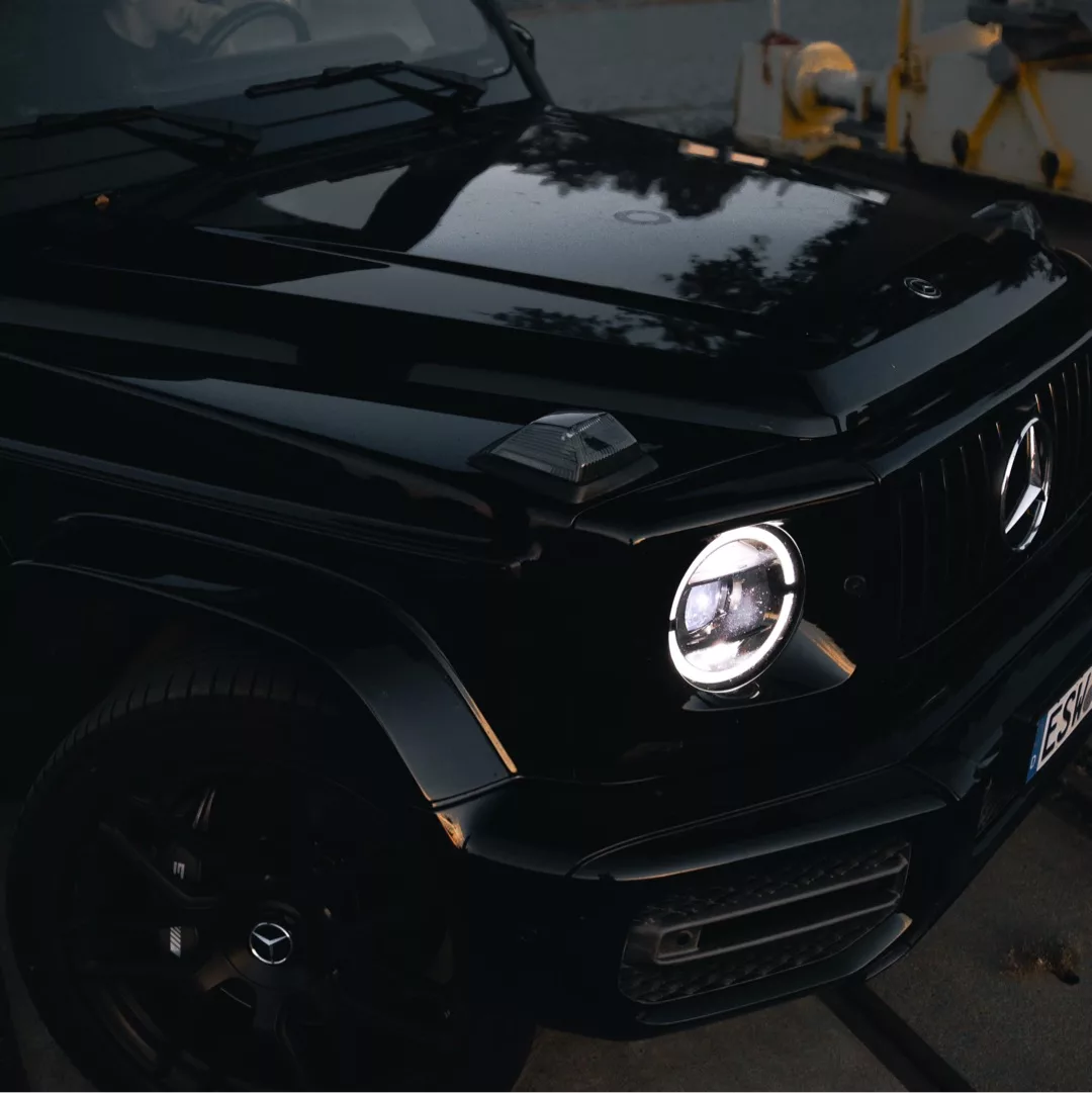 Mercedes G63 AMG in Schwarz mit eingeschaltetem Scheinwerfer mieten.