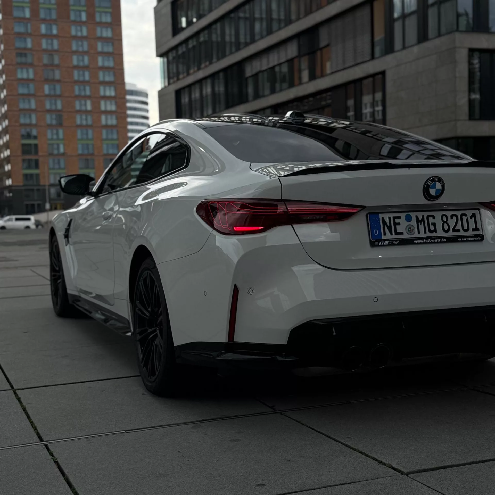 BMW M4 Competition in Weiß, Heckansicht auf urbanem Hintergrund mieten.