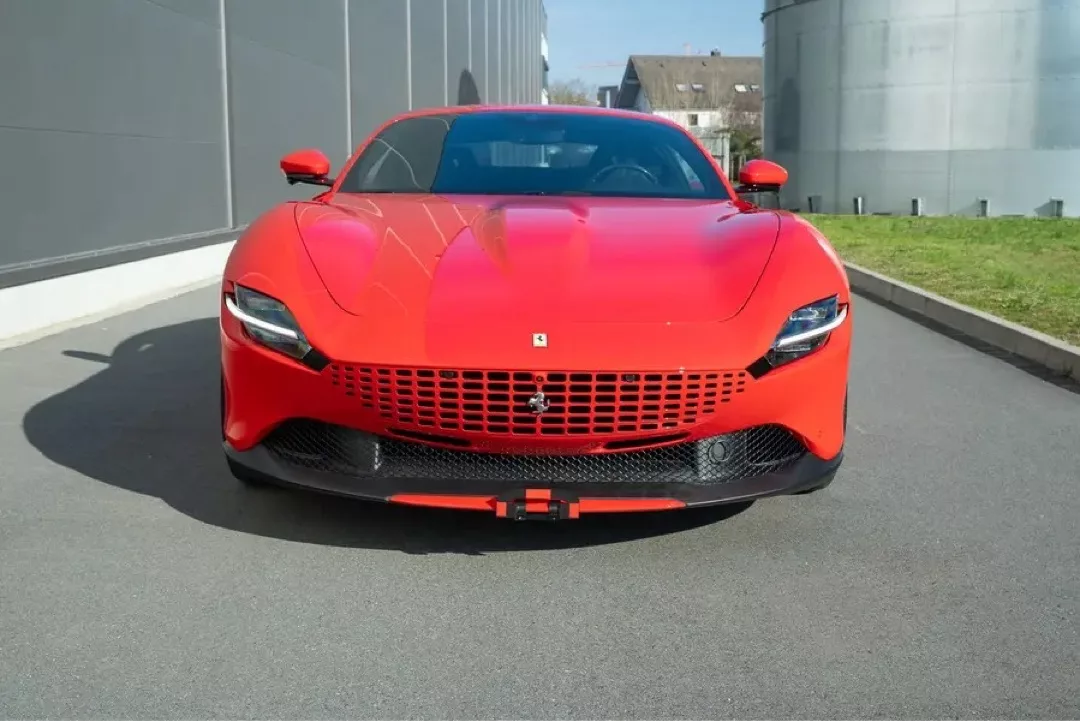 Roter Ferrari Roma auf einer Straße vor einer modernen Gebäudewand.
