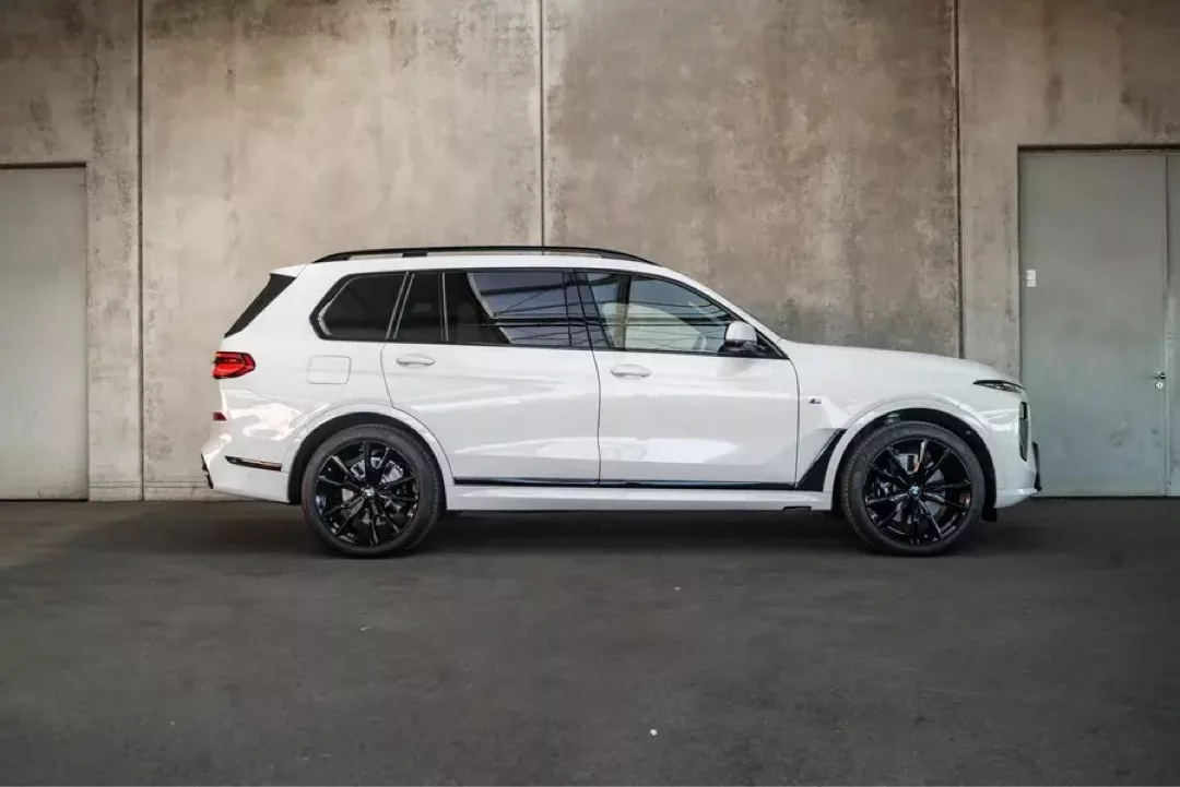 Weißer BMW X7 SUV mit schwarzen Felgen vor einer Betonwand.