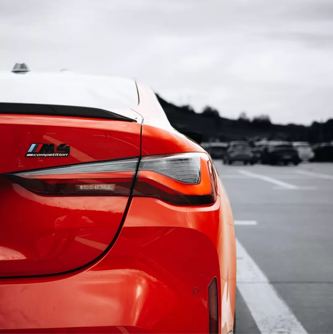 Roter BMW M4 Competition xDrive auf einer Straße von hinten fotografiert.