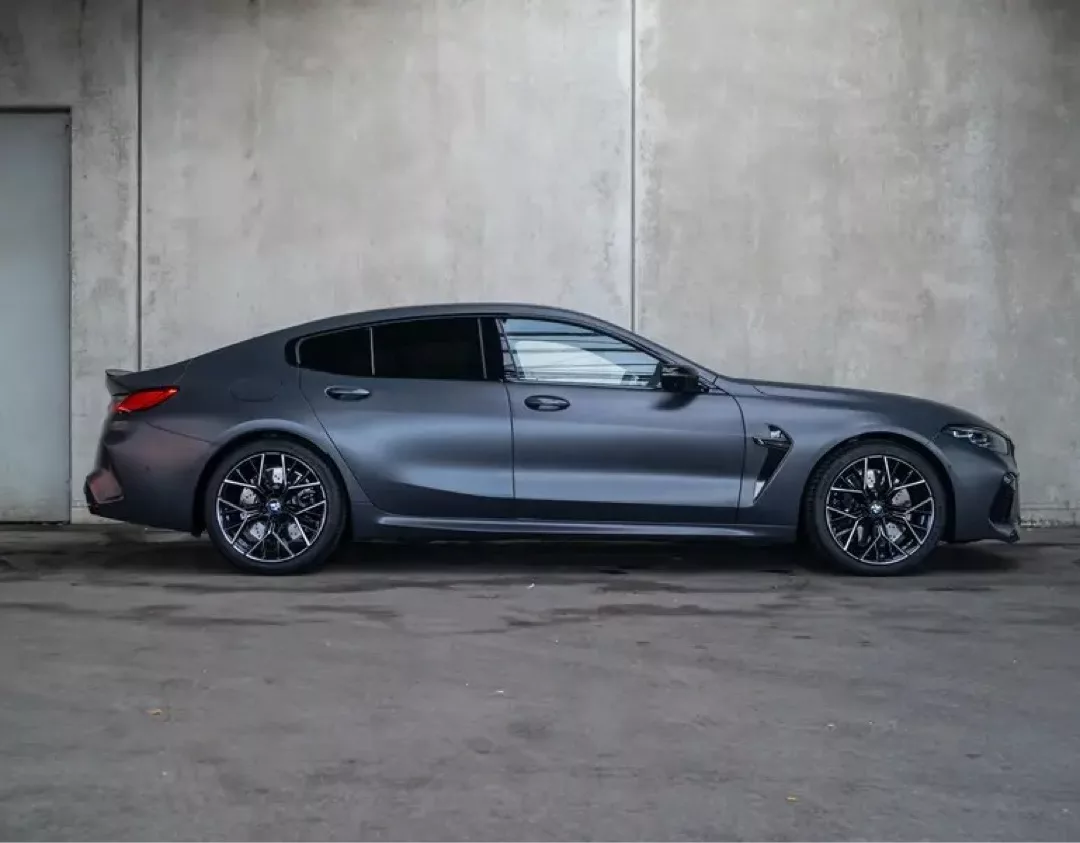 BMW M8 Gran Coupé in mattem Grau vor Betonwand.