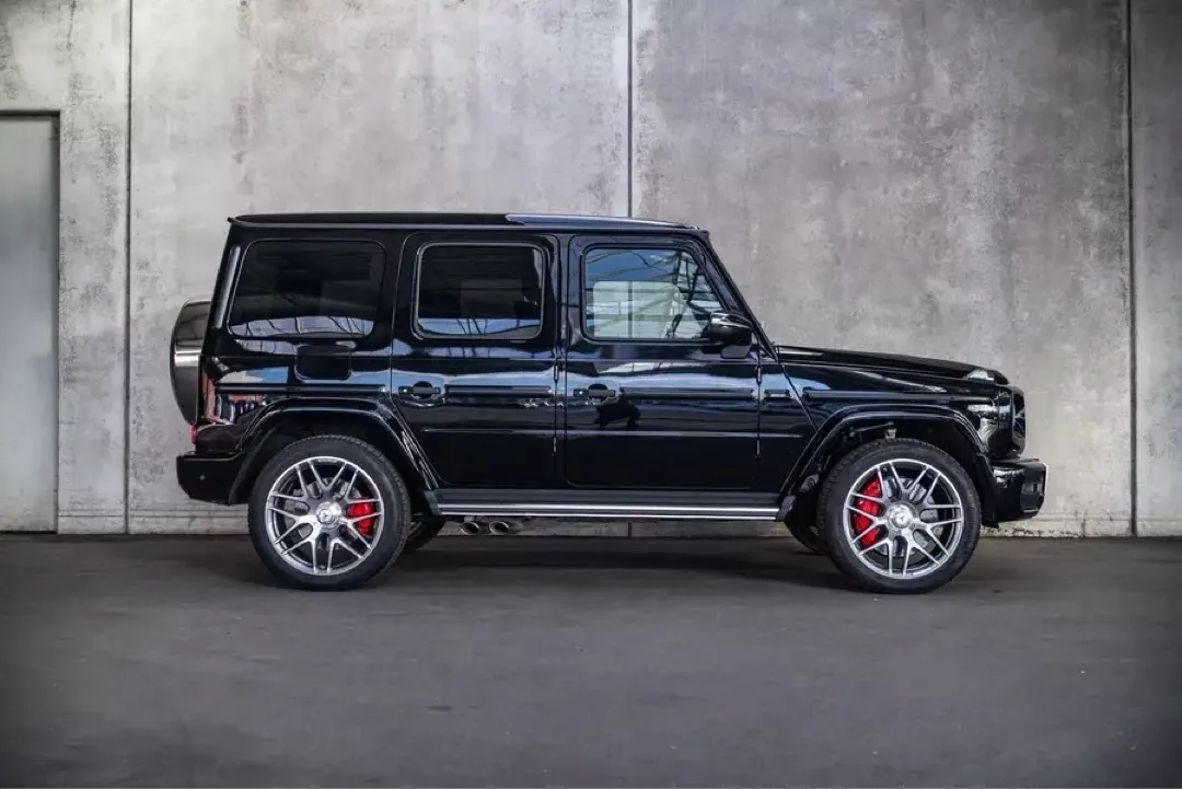 Schwarz glänzender Mercedes-Benz G63 AMG vor einer grauen Wand.