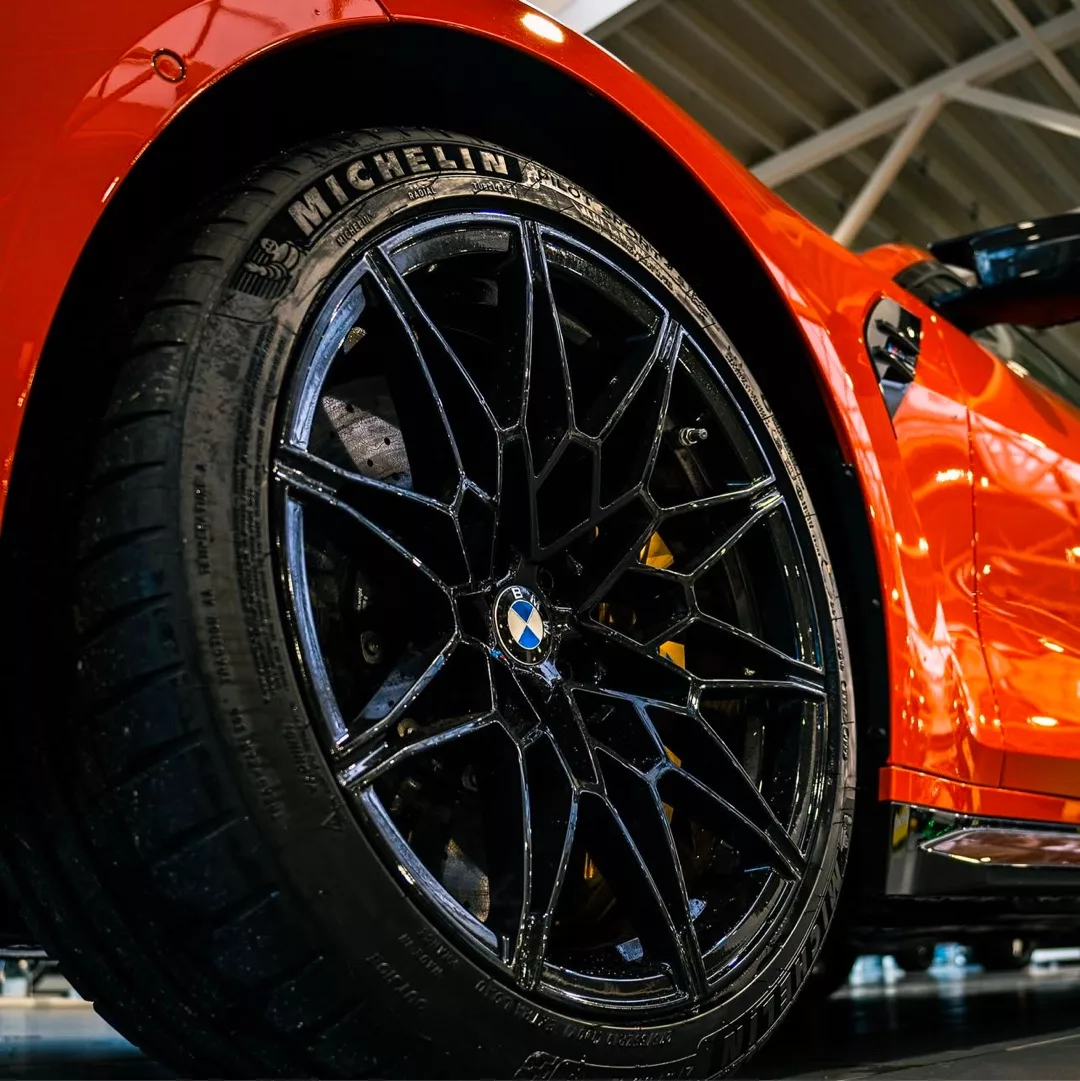 BMW M4 Competition in Orange mit Nahaufnahme der Felgen mieten.
