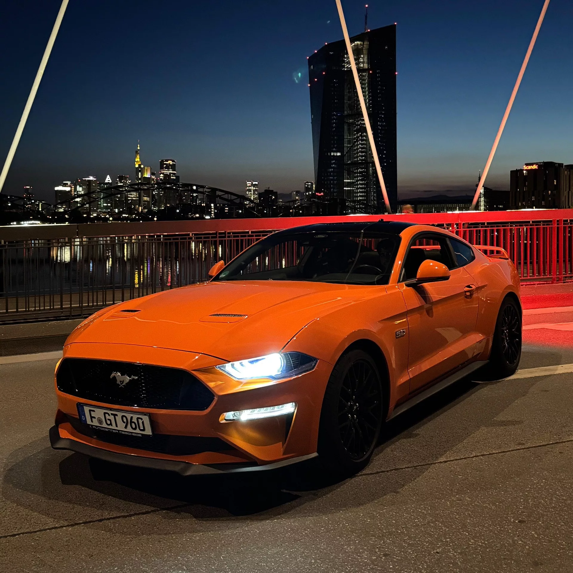 Ford Mustang GT in Orange bei Nacht vor Skyline mieten
