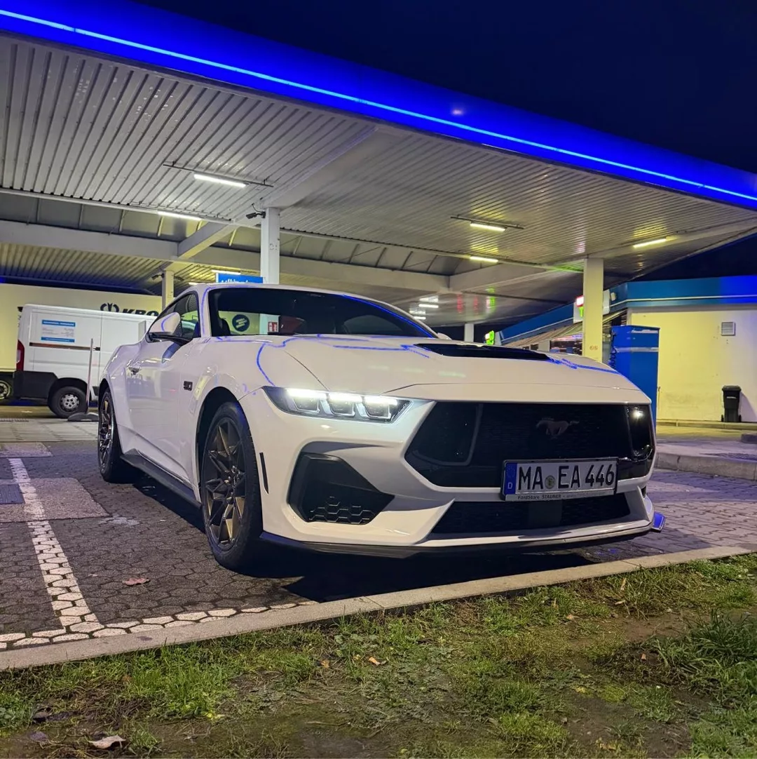 Ford Mustang GT in Weiß bei Nacht mieten - Frontansicht an Tankstelle.