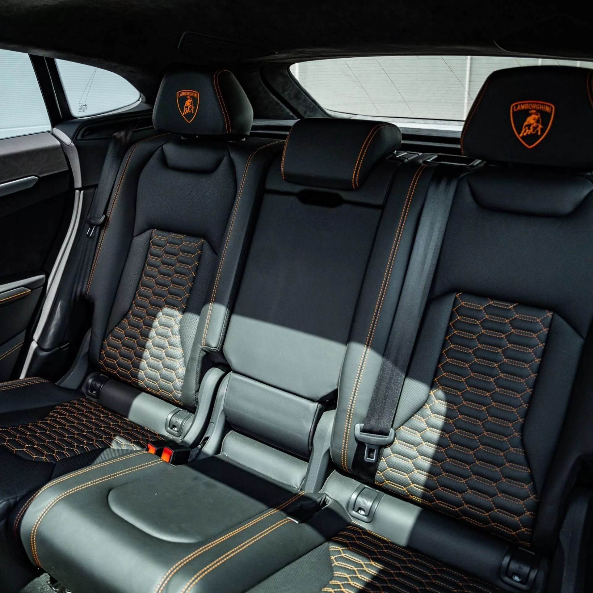 Rücksitze eines Lamborghini Urus mit schwarzer Lederpolsterung und orangefarbenen Nähten.