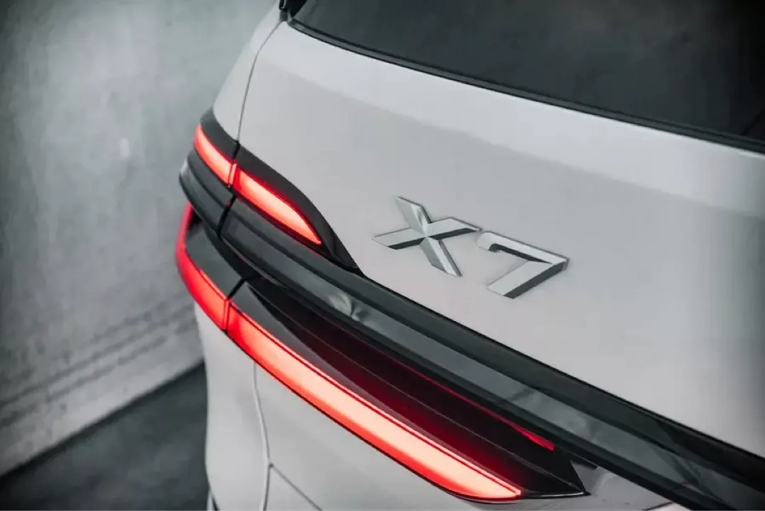 Rückansicht eines weißen BMW X7 mit leuchtenden Rücklichtern.