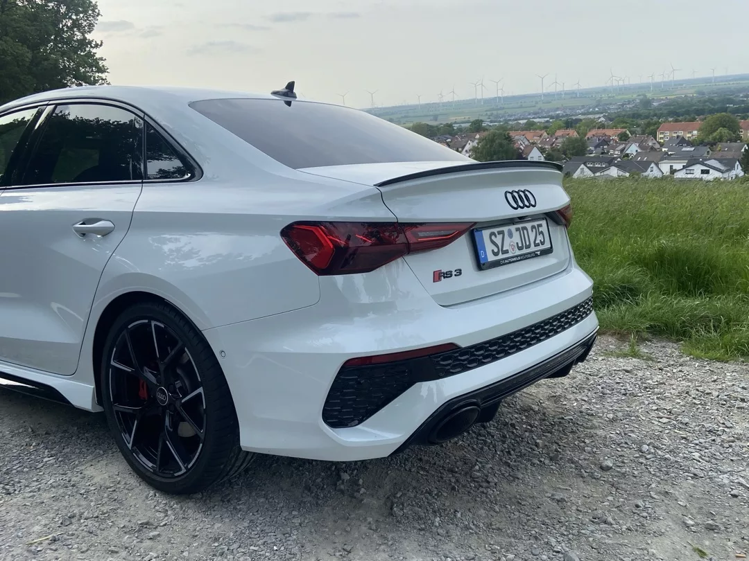 Audi RS3 Limousine in Weiß, Heckansicht auf Schotterweg mieten.