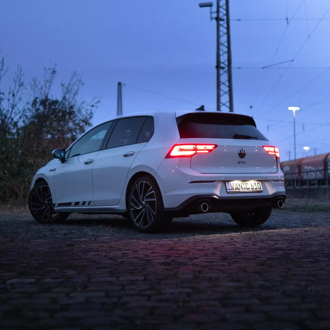 VW Golf 8 GTI in Weiß von hinten bei Abenddämmerung mieten